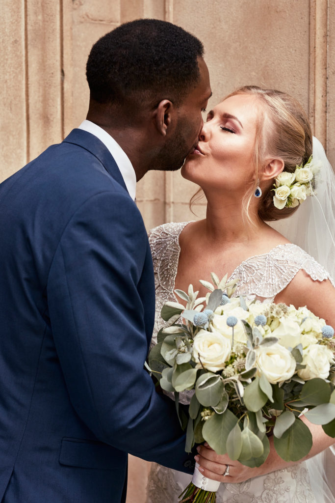 Bride and groom kissing with her bouquet of white roses in the foreground